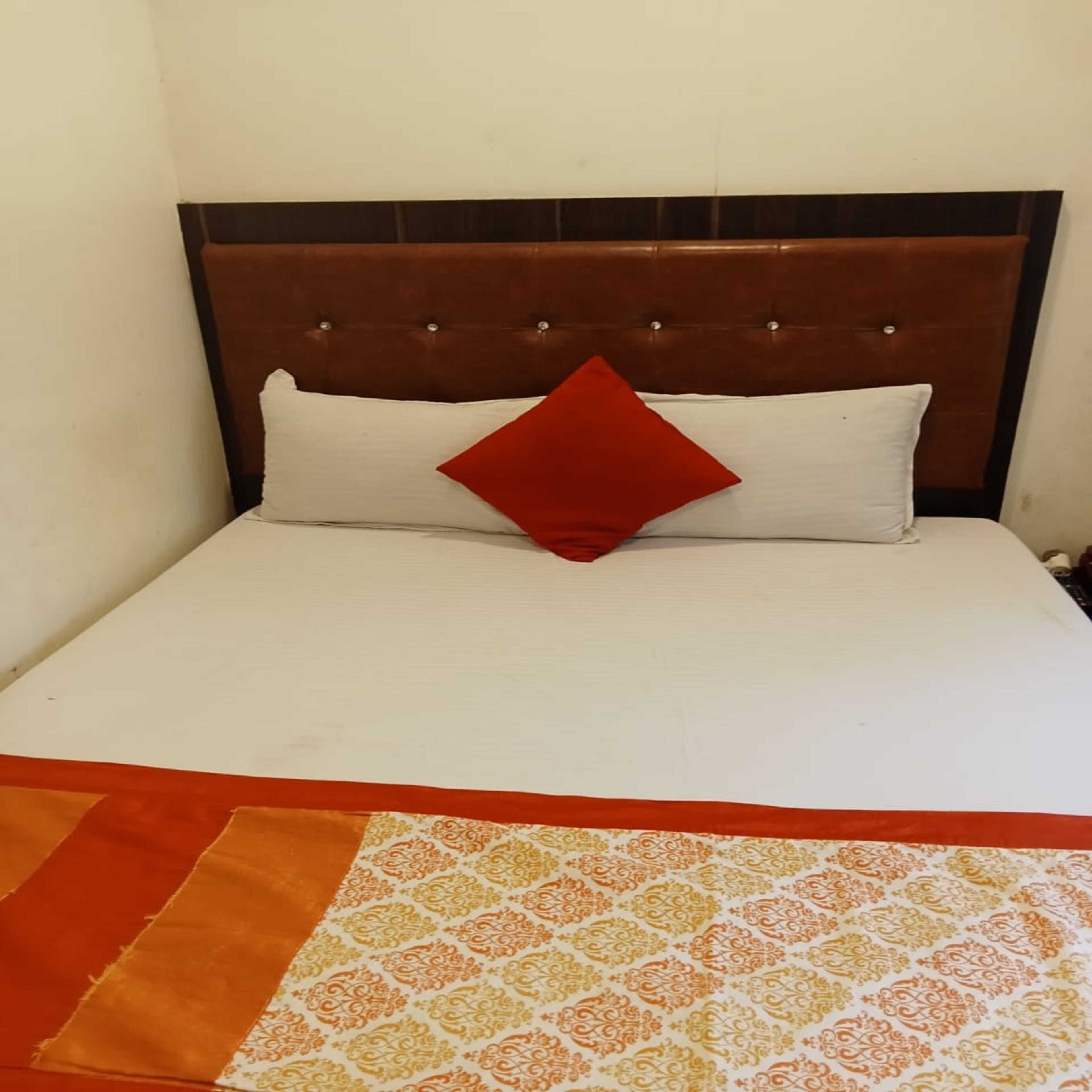 Ein Bett mit braunem Kopfteil, weißer Bettwäsche und einem roten Kopfkissen.