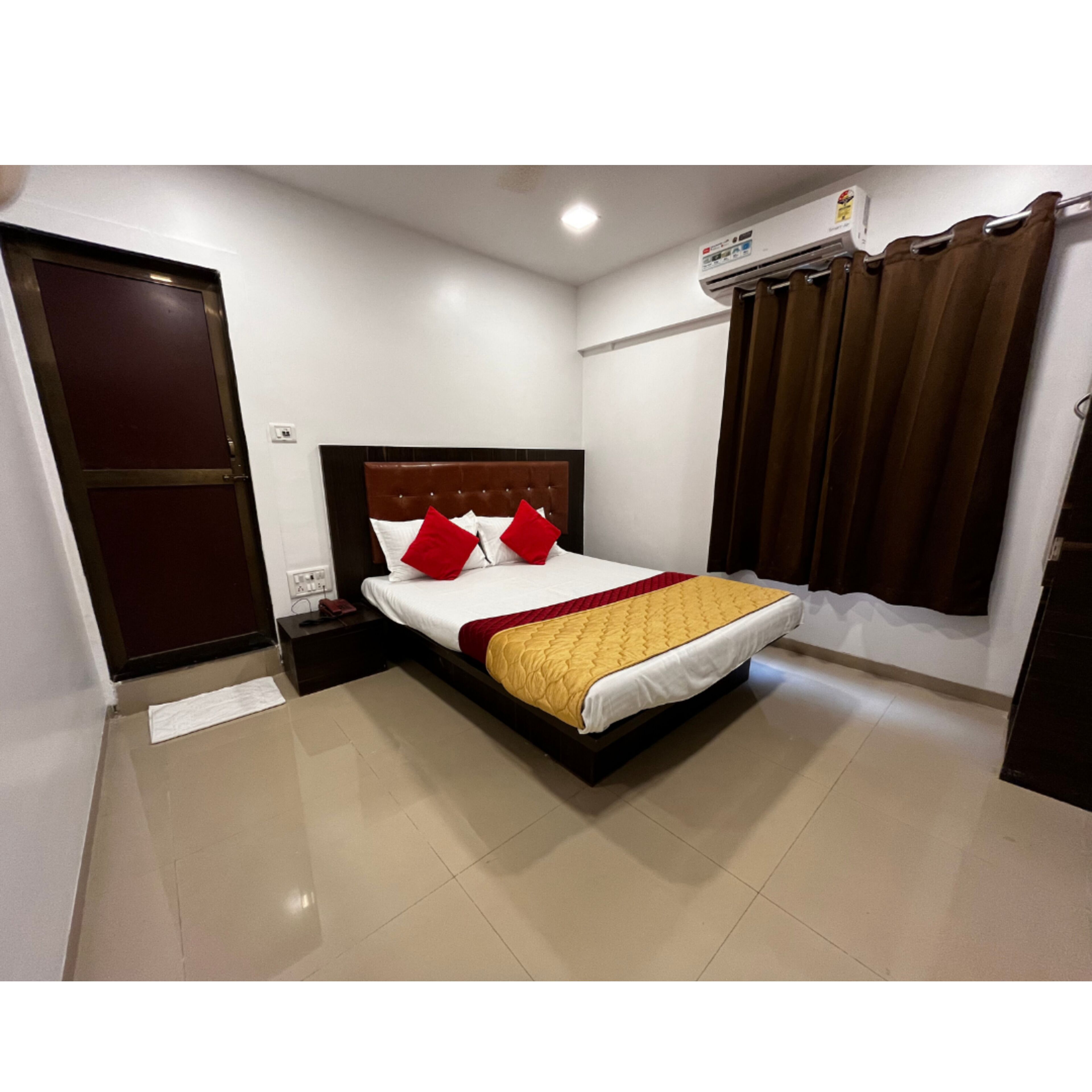 A hotel room with a bed, a nightstand, an air conditioning unit, and a door.
