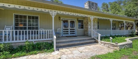 A yellow building with a porch, stone steps, and a stone chimney.