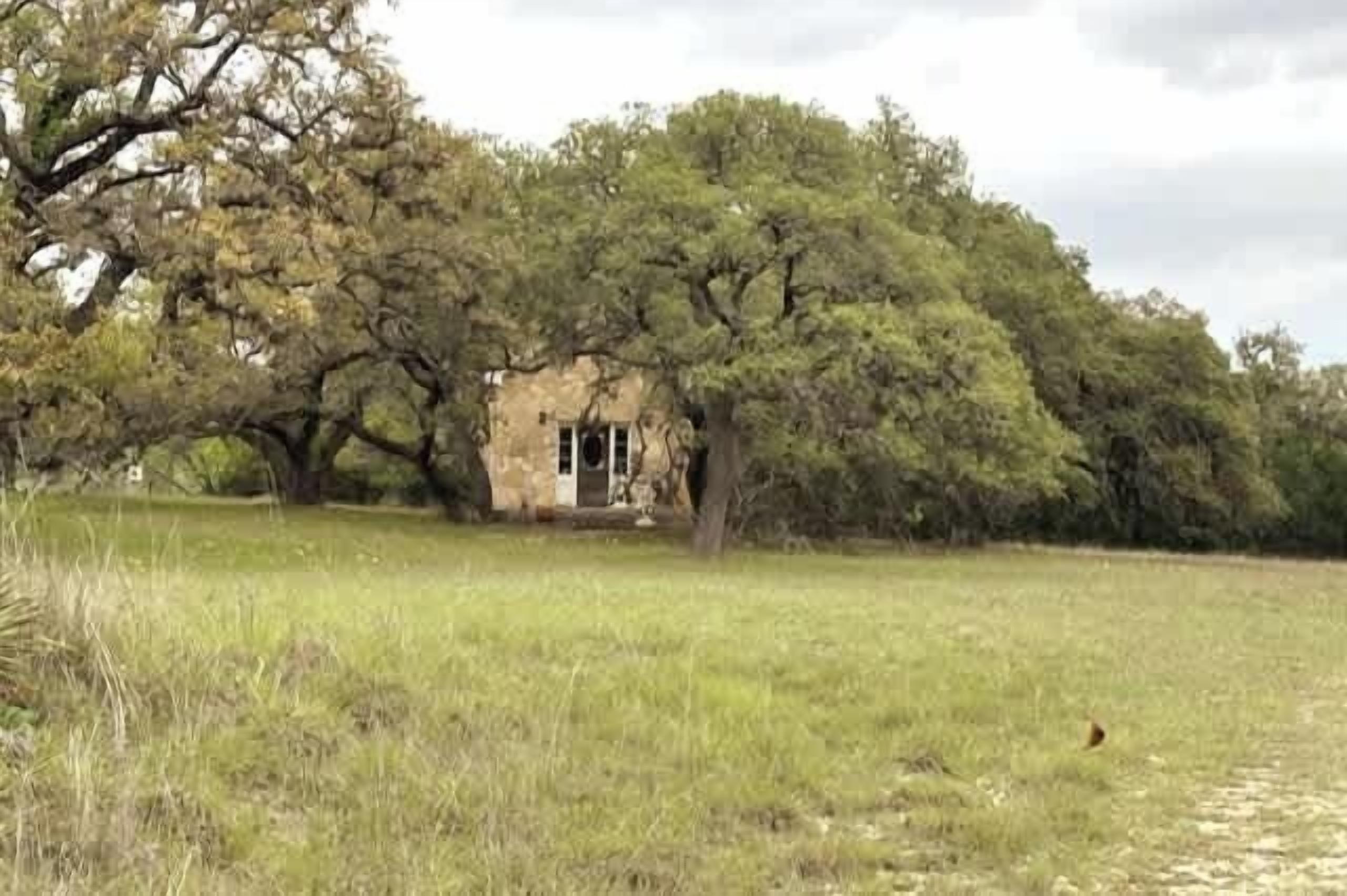 Un edificio de piedra rústico rodeado de árboles frondosos en un campo cubierto de hierba.