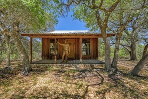 A wooden cabin with a porch, surrounded by trees. - Stunninghome on The Blanco River (Blanco)