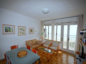 A living room with a sofa, chairs, a glass-top table, and framed pictures on the wall.