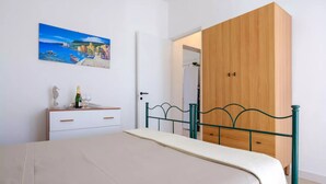 A bedroom with a bed, a wooden wardrobe, a white dresser, a painting, and a bottle of champagne. - Villa Punta Prosciutto Sea View Sea Front (Porto Cesareo)