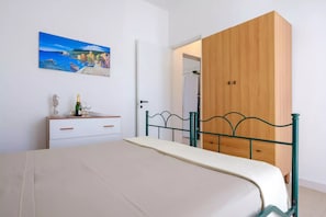 A bedroom with a bed, a wooden wardrobe, a white dresser, a painting, and a bottle of champagne. - Villa Punta Prosciutto Sea View Sea Front (Porto Cesareo)
