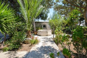 A garden pathway leading to a building with an arched entrance, surrounded by various plants and trees. - Villa Punta Prosciutto Sea View Sea Front (Porto Cesareo)