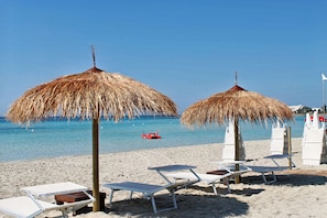 A beach with thatched umbrellas, lounge chairs, and a clear blue sea.