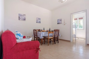A dining area with a table set for four, surrounded by chairs, and a red sofa in the foreground. - Villa Punta Prosciutto Sea View Sea Front (Porto Cesareo)