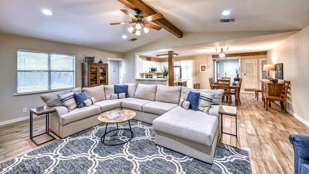 A spacious living area with a large L-shaped sectional sofa, a dining table with chairs, and a ceiling fan. - The Billie Goat Haus - Hot Tub -steps to Main St! (Fredericksburg)
