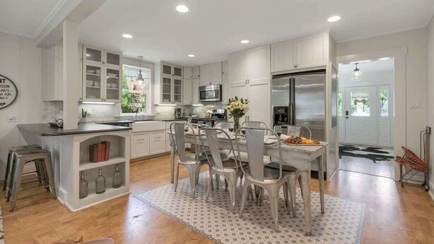 A modern kitchen with white cabinetry, a central island, and a dining area with metal chairs. - Clover Haus 2 Blks to Main St With Pool and Spa! (Fredericksburg)