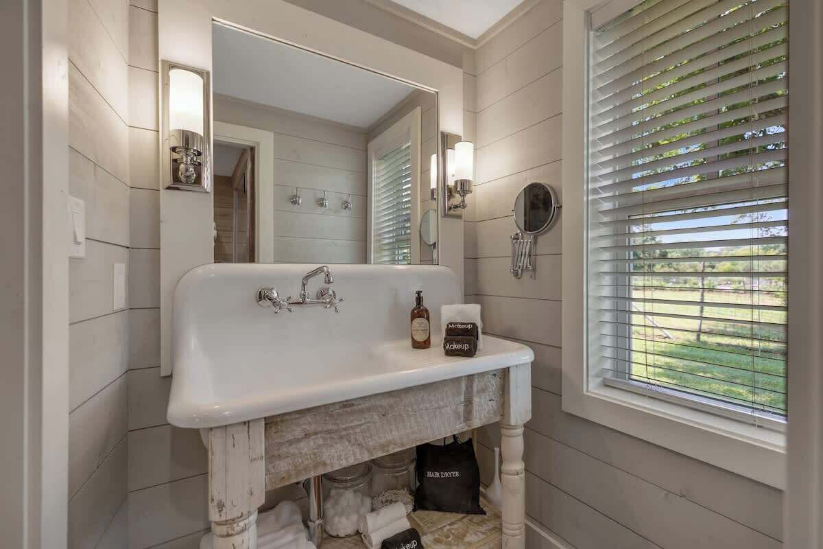 Un baño con un lavabo blanco, un espejo y una ventana con persianas.