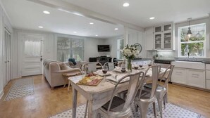 A spacious kitchen with white cabinets, a dining table set for six, and a cozy seating area with a sofa and chairs. - Clover Haus 2 Blks to Main St With Pool and Spa! (Fredericksburg)