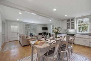 Una cocina amplia con armarios blancos, una mesa de comedor preparada para seis personas y una zona de estar acogedora con sofá y sillones.