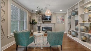 A living room with teal patterned chairs, a round table, a decorative vase, a fireplace, and a globe collection on shelves. - Clover Haus 2 Blks to Main St With Pool and Spa! (Fredericksburg)