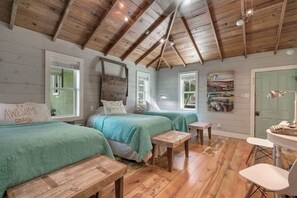Una habitación acogedora con pisos de madera, dos camas con ropa de cama verde, una mesita y una silla.