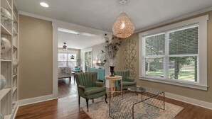 A spacious living room with a wooden floor, a green armchair, a round coffee table, and a decorative wall piece. - Clover Haus 2 Blks to Main St With Pool and Spa! (Fredericksburg)