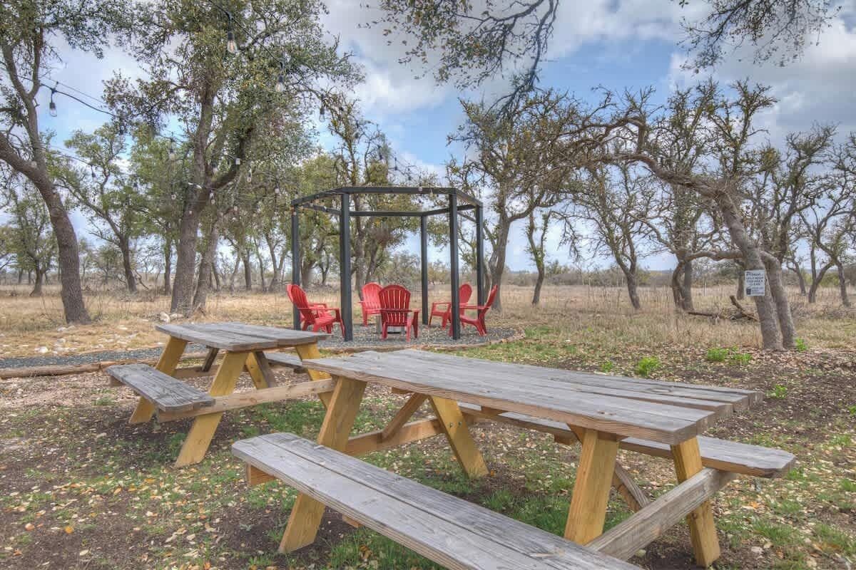 Un área de picnic con bancos de madera y sillas rojas, rodeada de árboles.
