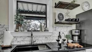 A modern kitchen with a marble backsplash, a stainless steel sink, a coffee machine, and a window with a view of trees. - Hill Country Hideaway With Fire Pit and Hot Tub! (Fredericksburg)