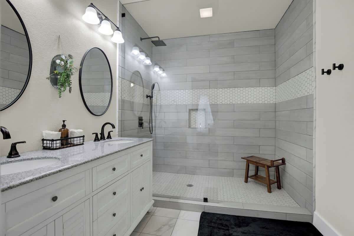 A modern bathroom with a vanity, two mirrors, a shower with a glass door, and a small wooden stool.