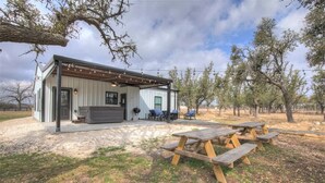 A rustic cabin with a covered patio, outdoor seating, and a picnic table area. - Hill Country Hideaway With Fire Pit and Hot Tub! (Fredericksburg)