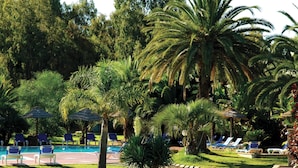 A pool area with lounge chairs and umbrellas, surrounded by palm trees and greenery. - Fantastico Baia de Bahas Residence Sea View 2 Bedroom Sleeps 6 (Golfo Aranci)