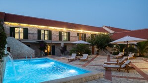 A stone pool with lounge chairs and umbrellas, a stone building with a red-tiled roof, and a staircase leading to a balcony. - Villa Jokić Dvori (Benkovac)
