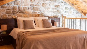 A bedroom with a stone wall, wooden ceiling, and a bed with multiple pillows. - Villa Jokić Dvori (Benkovac)