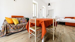 A room with a dining table, a sofa with colorful cushions, a bed with orange bedding, and a wooden floor. - Via Morghen 63 - Primo Piano (Naples)
