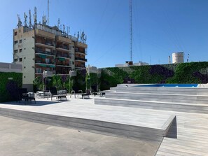A rooftop terrace with a pool, outdoor seating, and a building with multiple balconies in the background. - Brand New Apartment In Caballito (Buenos Aires)