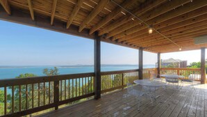 Una terraza de madera con vista al mar, sillas de metal y una mesa.