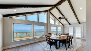 Un comedor amplio con una mesa grande y sillas, ventanas panorámicas con vista al océano y un ventilador de techo.
