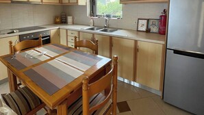 Una cocina con armarios de madera, un refrigerador de acero inoxidable, una mesa de comedor con sillas y una ventana que proporciona luz natural.