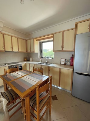 A kitchen with wooden cabinets, a stainless steel refrigerator, a dining table with chairs, and a window providing natural light. - The Pearl Seaview Apartment, 10sec Walk To The Sea (Messini)
