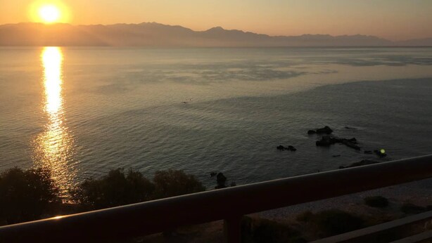 Un atardecer sobre aguas tranquilas con montañas a lo lejos.