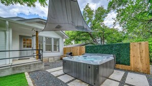 A hot tub in a backyard with a house, a wooden fence, and a green hedge.