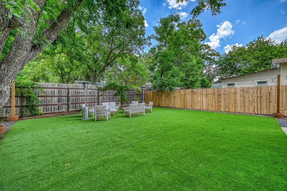 Un jardin avec une clôture en bois, une pelouse verdoyante et du mobilier d’extérieur.