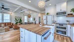 A modern kitchen with white cabinetry, a central island with a wooden countertop, and built-in appliances including a microwave and oven.