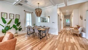 A spacious dining area with a wooden floor, a chandelier, and a dining table set for six.