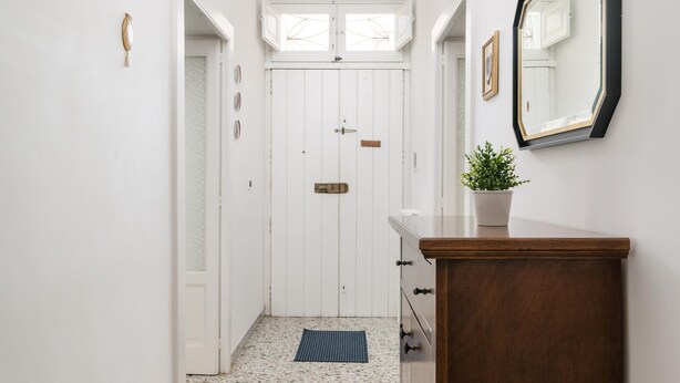 A hallway with a wooden dresser, a potted plant, and a mirror on the wall.