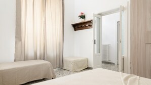 A bedroom with two beds, a wooden shelf with a vase, and a door leading to another room.