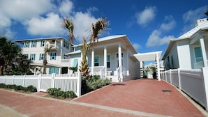 A coastal property with a paved walkway, white fences, and a clear blue sky.