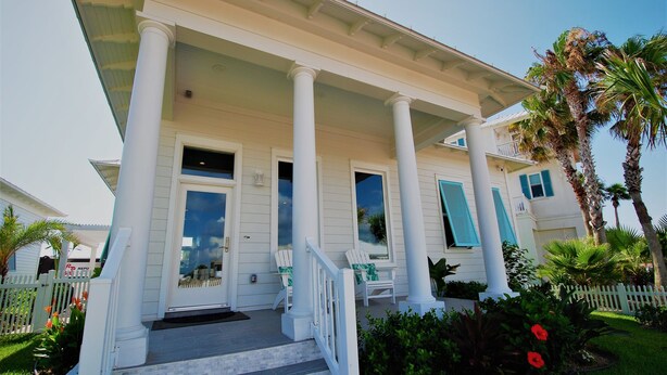 A two-story house with a porch, white columns, and a white picket fence.
