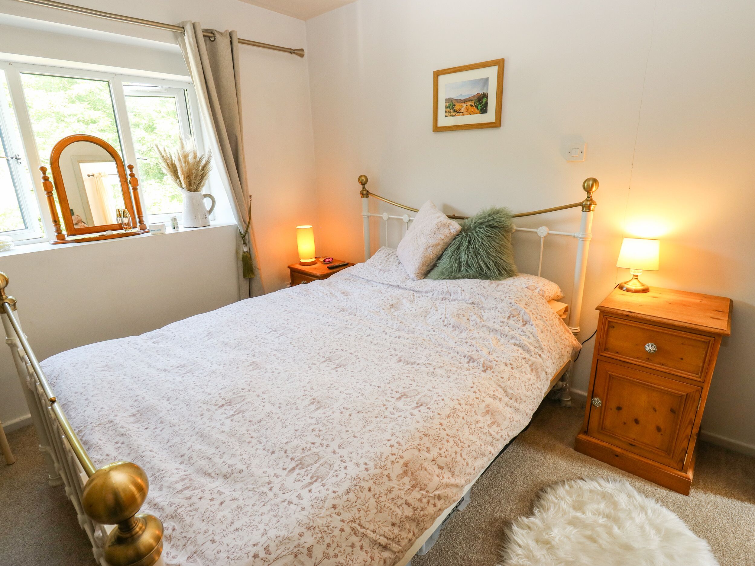 Un dormitorio con cama, lámparas de noche, mesita de noche, espejo, ventana con cortinas e imagen enmarcada en la pared.