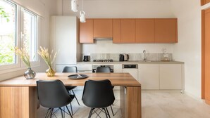 A modern kitchen with white and wooden cabinets, a dining table with chairs, and a window with a view of greenery.