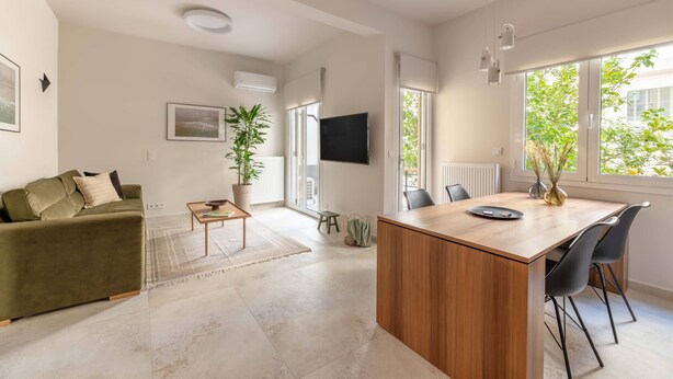 A modern living room with a sofa, a coffee table, a TV, and a dining area with chairs and a table.