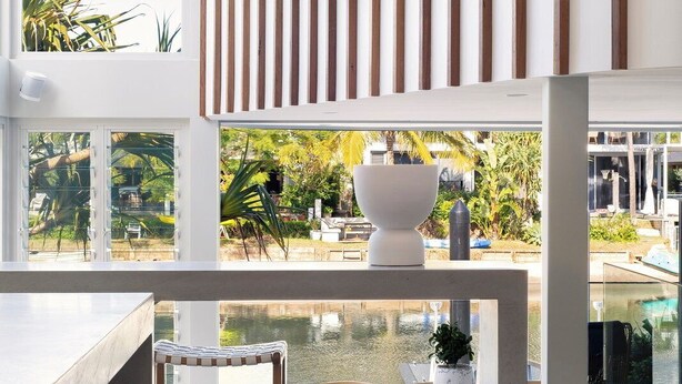Un intérieur moderne donnant sur une piscine, avec des meubles en bois et un plafond blanc agrémenté de lambris en bois verticaux.