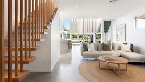 Un salon moderne avec un escalier, un canapé, une table basse et une vue sur l’extérieur.