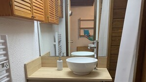 Ein kleines Badezimmer mit einem Holzbadezimmer-Möbel, einem großen Spiegel und einem weißen Waschbecken.