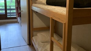 Ein Schlafraum mit Etagenbett, Holzrahmen, weißer Bettwäsche und einer Tür zu einem Balkon mit Blick auf Grünflächen.