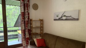 Ein gemütliches Wohnzimmer mit einem braunen Sofa, roten und weißen Kissen, einer Holzleiterregal und einem Bild von Pflanzen.