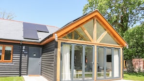 A modern house with a large glass door, a small attached garage, and a sloped roof with solar panels. - Robins Nest (Fareham)